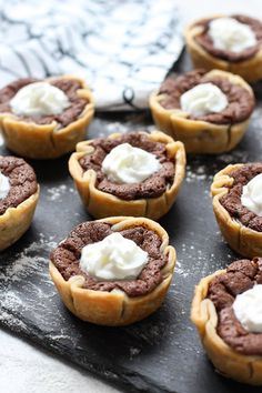 chocolate cupcakes with whipped cream are sitting on a black slate board next to a knife