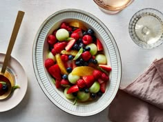 a bowl filled with fruit on top of a table next to plates and utensils