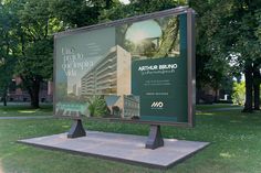 a large sign in the middle of a grassy area with trees and buildings behind it