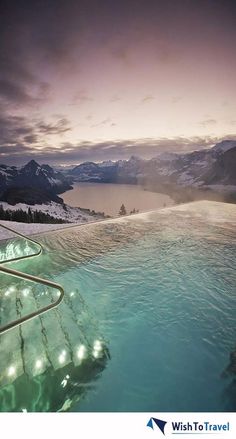 an image of a hot tub in the water with lights on it and mountains in the background