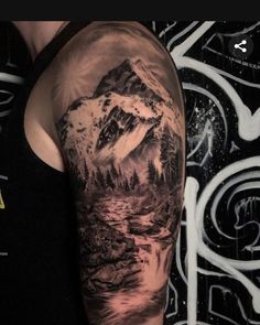 a man's arm with a mountain scene on it and water in the background