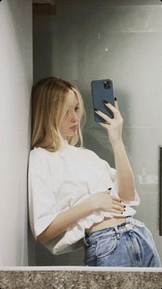 a woman is taking a selfie with her cell phone in the bathroom while wearing jeans