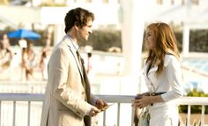 a man and woman standing next to each other on a balcony near the ocean with people in the background