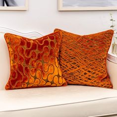 two orange pillows sitting on top of a white couch next to a vase with flowers