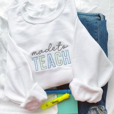 a white sweatshirt with the words made to teach on it next to some school supplies