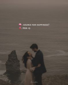 a man and woman standing next to each other on top of a cliff near the ocean