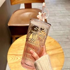 a person holding up a starbucks cup with a straw in it on a table next to a chair