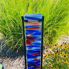 a blue and red vase sitting on top of a table next to some flowers in a garden