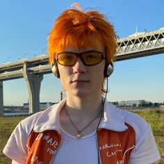 a young man with orange hair wearing headphones and ear phones in front of a bridge