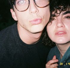 a man and woman are posing for a photo together, one is wearing glasses the other has curly hair