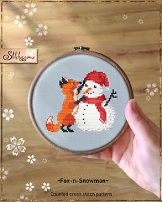 a hand holding up a cross stitch pattern with a snowman and fox on it