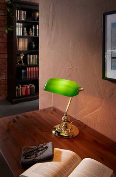 an open book sitting on top of a wooden table next to a green desk lamp