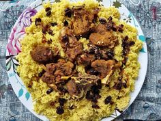 a white plate topped with rice and meat on top of a floral table cloth next to utensils