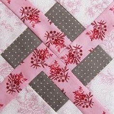 a pink and gray patchwork quilt with red flowers on the center is laying flat