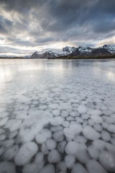 an icy lake surrounded by snow covered mountains and clouds in the distance, with ice floes floating on the water