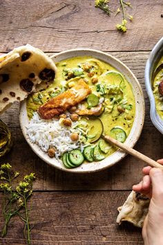 a bowl of food with rice, meat and cucumbers in it on a wooden table