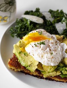 an egg and avocado toast on a white plate next to some salad greens