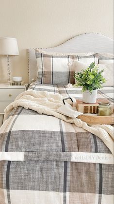 a bed with a plaid comforter and pillows on it, next to a small potted plant