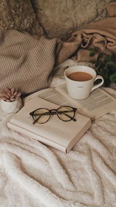 an open book and cup of coffee sit on a bed next to a blanket with a plant