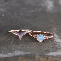 two rings with opal and diamond accents on top of a stone surface in front of a brick wall