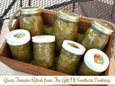 four jars filled with green tomato relish sit in a wooden box on a table