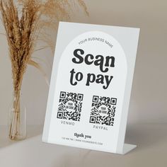 a sign that says scan to pay next to a vase with dried grass in it