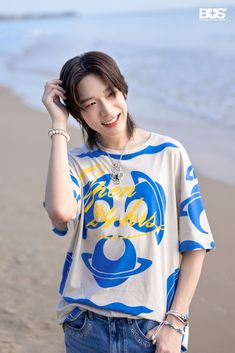 a young woman standing on top of a beach next to the ocean holding a cell phone