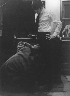 a black and white photo of a man in a suit leaning against a luggage bag