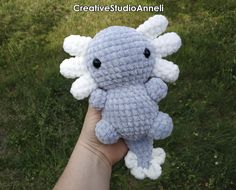 a hand holding a crocheted blue and white stuffed animal in the middle of grass