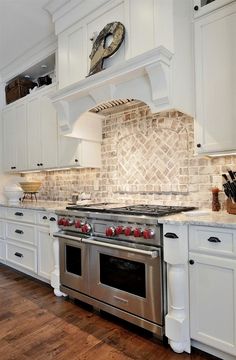 a kitchen with white cabinets and stainless steel stove top oven in front of a clock on the wall