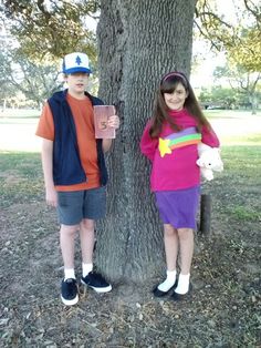 two people standing next to each other near a tree with a book in their hands