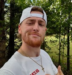 a man in a white shirt giving the thumbs up with trees and grass behind him