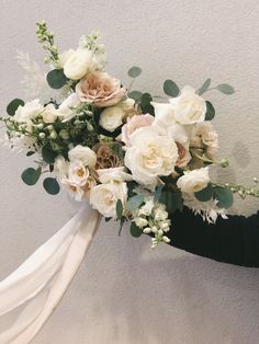 a bridal bouquet with white flowers and greenery is held by a woman's arm