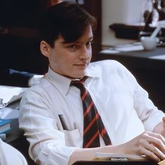 a man wearing a white shirt and tie sitting at a desk with a binder on his lap