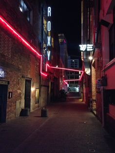 an alley way with red neon lights on the buildings