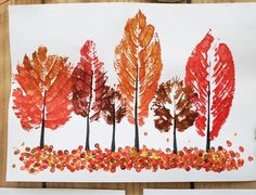 an art project with leaves painted on white paper and colored pencils next to it