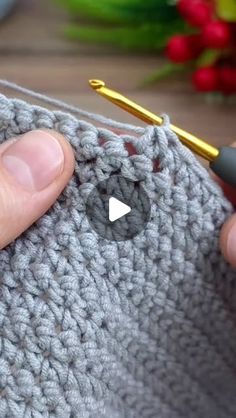 someone is crocheting the stitchs on a gray knitted object with a yellow knitting needle