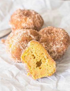 three sugar coated doughnuts sitting on top of a piece of wax paper next to a spoon