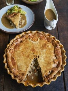 a pie with a slice missing from it on a wooden table next to other dishes