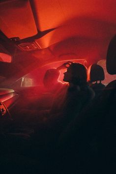 two people sitting in the passenger seat of a car with red light coming from behind them