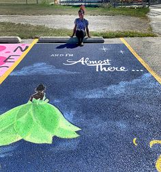 a woman sitting on the ground in front of a chalk drawing with a green dress