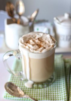 there is a cup of coffee with whipped cream in it and spoons on the table