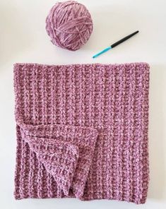 a crocheted blanket with two balls of yarn next to it and a ball of knitting needles