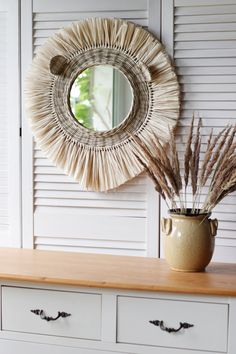 there is a vase with dried grass in it and a mirror hanging on the wall