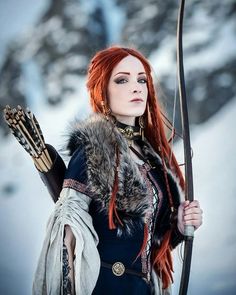 a woman with red hair holding a bow and arrow in her hand while standing on snow covered ground