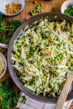 a pan filled with pasta and peas on top of a wooden table next to other dishes