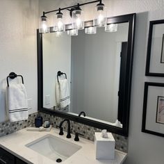 a bathroom sink with a large mirror and lights on the wall above it's counter