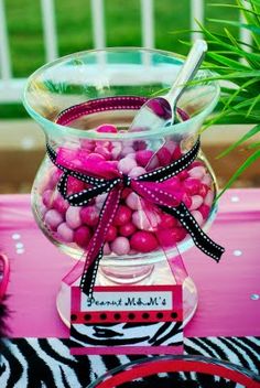 candy in a glass bowl on top of a zebra print table cloth with pink and black decorations