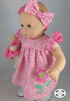 a baby doll wearing a pink dress and holding a teddy bear