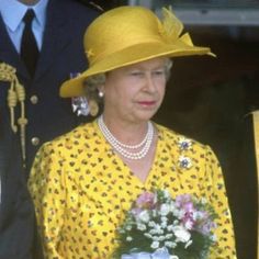 the queen is wearing a yellow hat and holding a bouquet of flowers in her hand